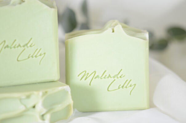 Four bars of Garden Mint soap displayed, with one standing upright and three stacked in front, showing their textured, natural surfaces. Fresh green foliage is visible in the background, adding to the soap's refreshing, botanical vibe.